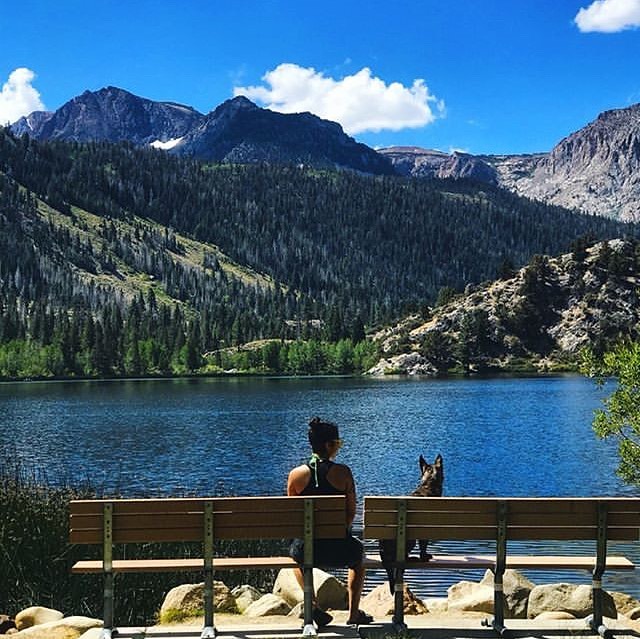 Yasmine Yousaf in a black jogging dress sitting by a lake with her dog. 